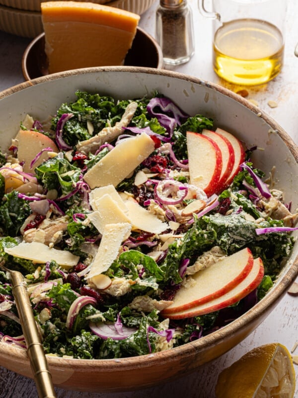 Kale chicken salad with sliced apples, parmesan cheese and a creamy dressing in a bowl.