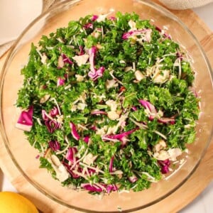 Kale chicken salad with red cabbage, red onion, parmesan cheese and a lemon vinaigrette in a large clear bowl.