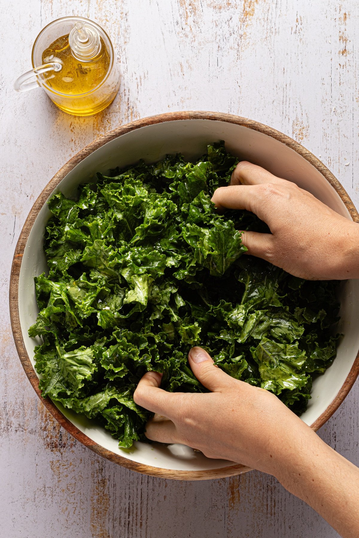 Kale being massaged in a bowl with olive oil.