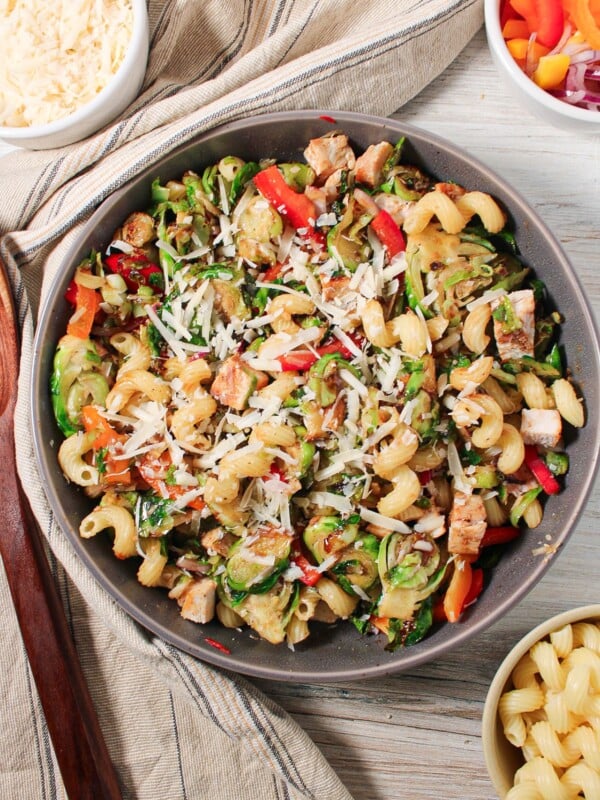A large bowl of brussel sprout pasta salad with pasta, brussels sprouts, peppers, onions, parmesan cheese and balsamic glaze.