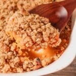 A close up shot of sweet potato casserole with walnut topping being scooped by a wooden spoon.