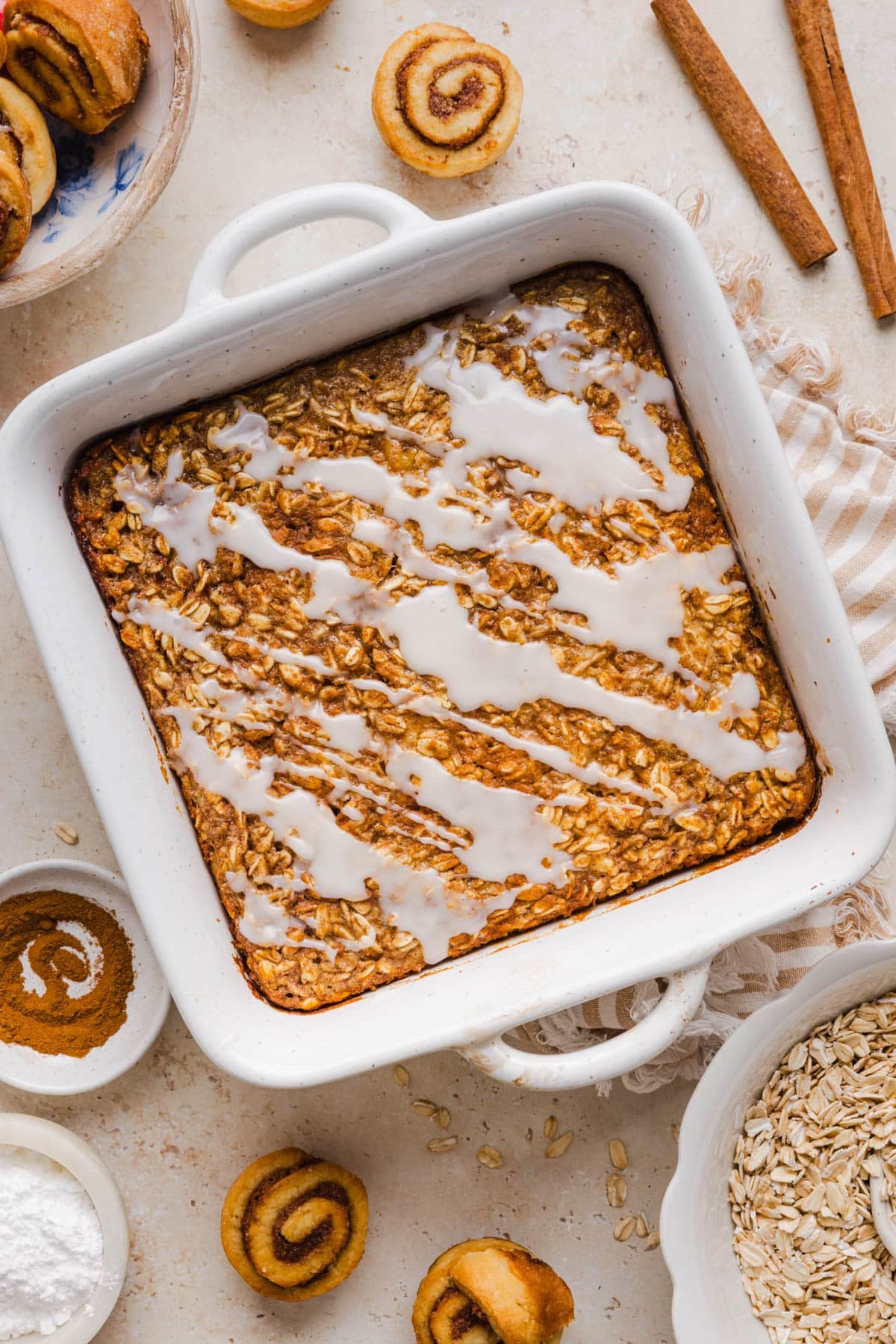 The baked cinnamon roll oatmeal drizzled with the glaze in the baking dish on a countertop.