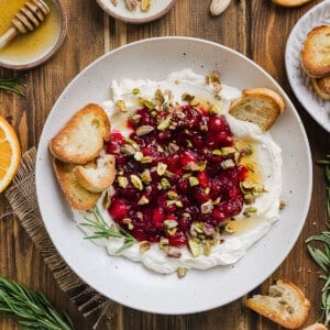 Whipped feta dip in a large bowl topped with homemade cranberry sauce and chopped pistachios and crostini.