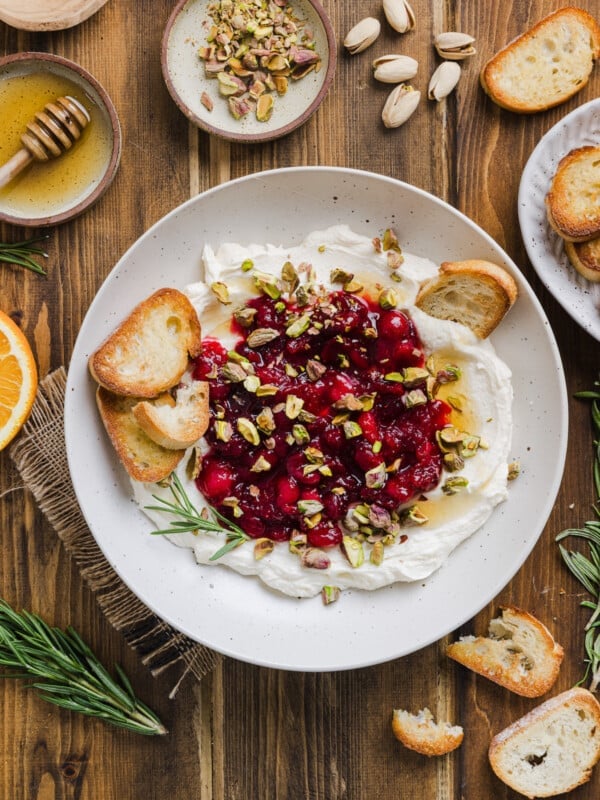 Whipped feta dip in a large bowl topped with homemade cranberry sauce and chopped pistachios and crostini.