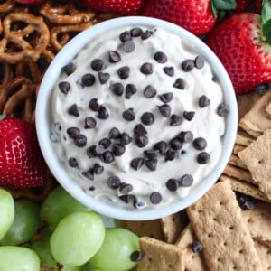 A close up shot of Greek yogurt cookie dough dip surrounded by strawberries, grapes, mini pretzels and graham cracker pieces.