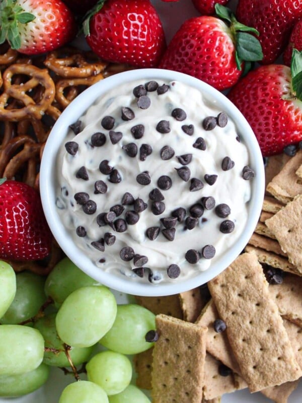 A close up shot of Greek yogurt cookie dough dip surrounded by strawberries, grapes, mini pretzels and graham cracker pieces.