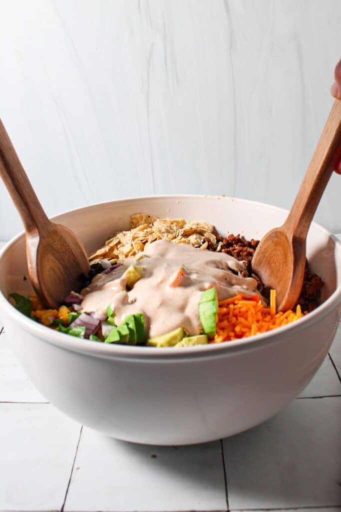 Ground beef salad unmixed in a bowl with dressing on top.