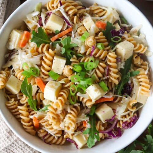 4 ingredient pasta salad in a white bowl garnished with green onions and arugula.