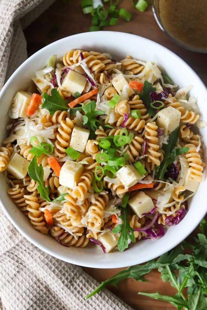 4 ingredient pasta salad in a white bowl garnished with green onions and arugula.