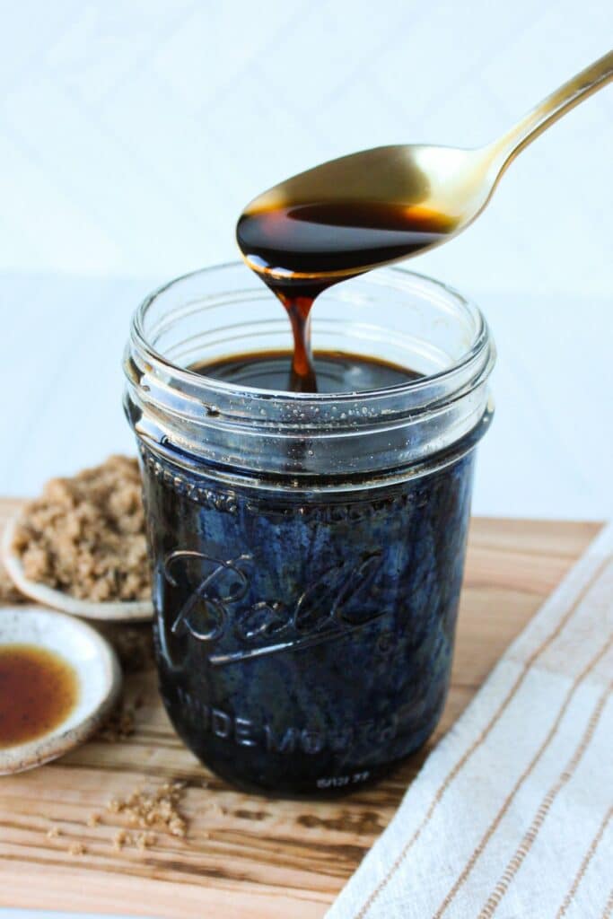 A spoon dripping brown sugar simple syrup into a mason jar.