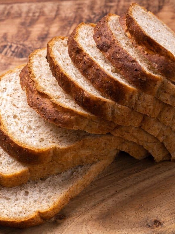 A loaf of sliced whole wheat bread on a wooden cutting board.