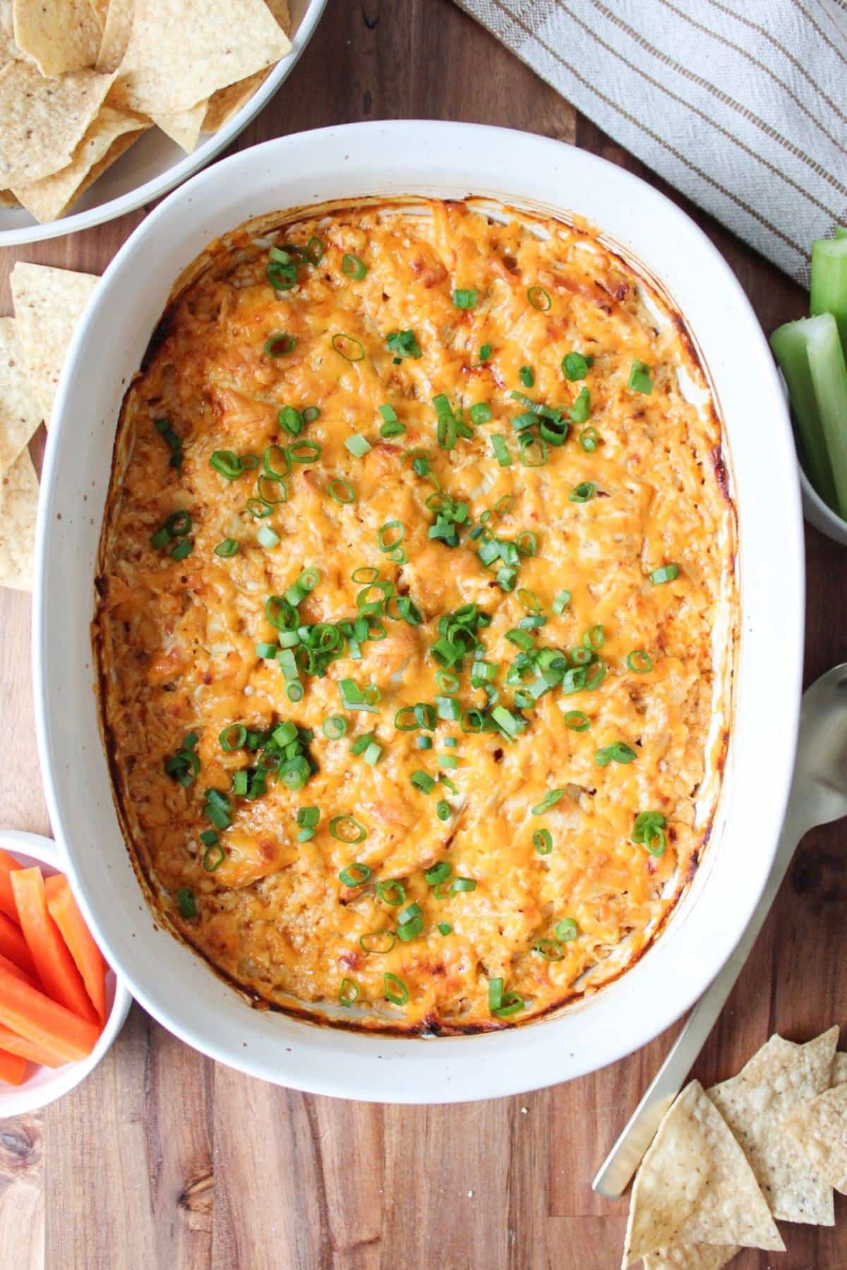 A large casserole dish full of high protein buffalo chicken dip with chips, celery and carrots.