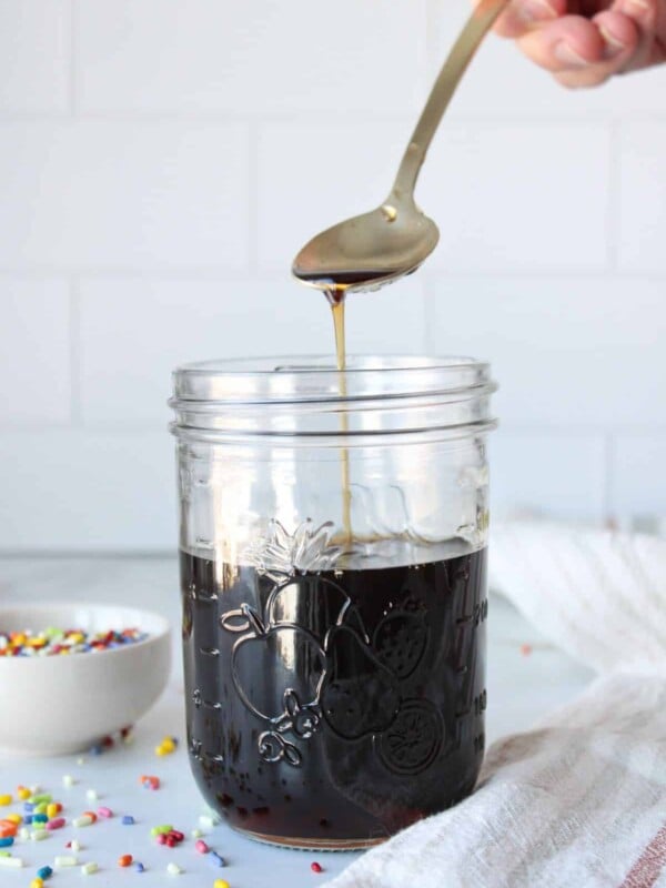 A mason jar full of sugar cookie cough syrup with a spoon dripping some into the jar.