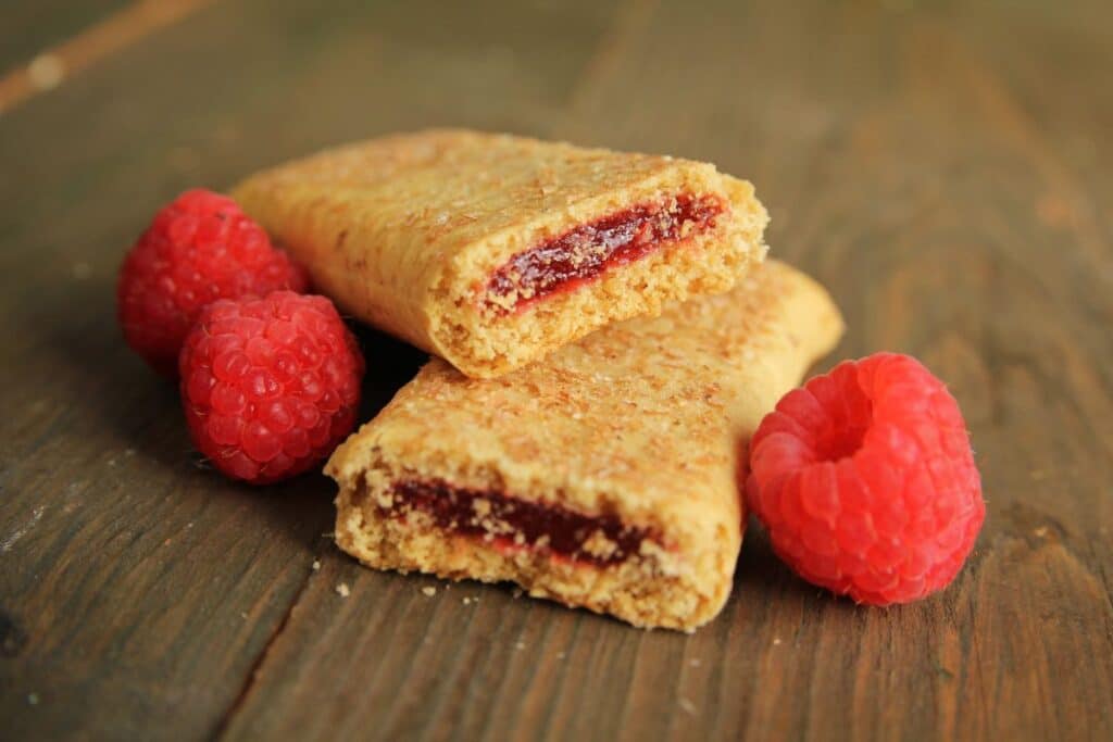 A cereal bar broken in half with raspberries.