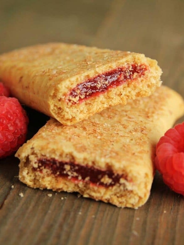A cereal bar broken in half with raspberries.