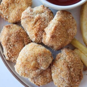 A close up shot of chicken nuggets with ground chicken, ketchup and french fries.