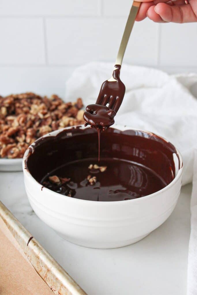 A fork lifting a chocolate covered walnut out of a bowl of melted chocolate.