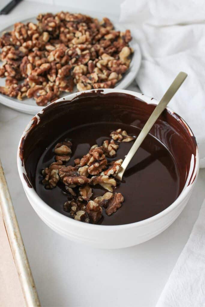 Walnuts in a bowl of melted chocolate ready to be coated in chocolate.