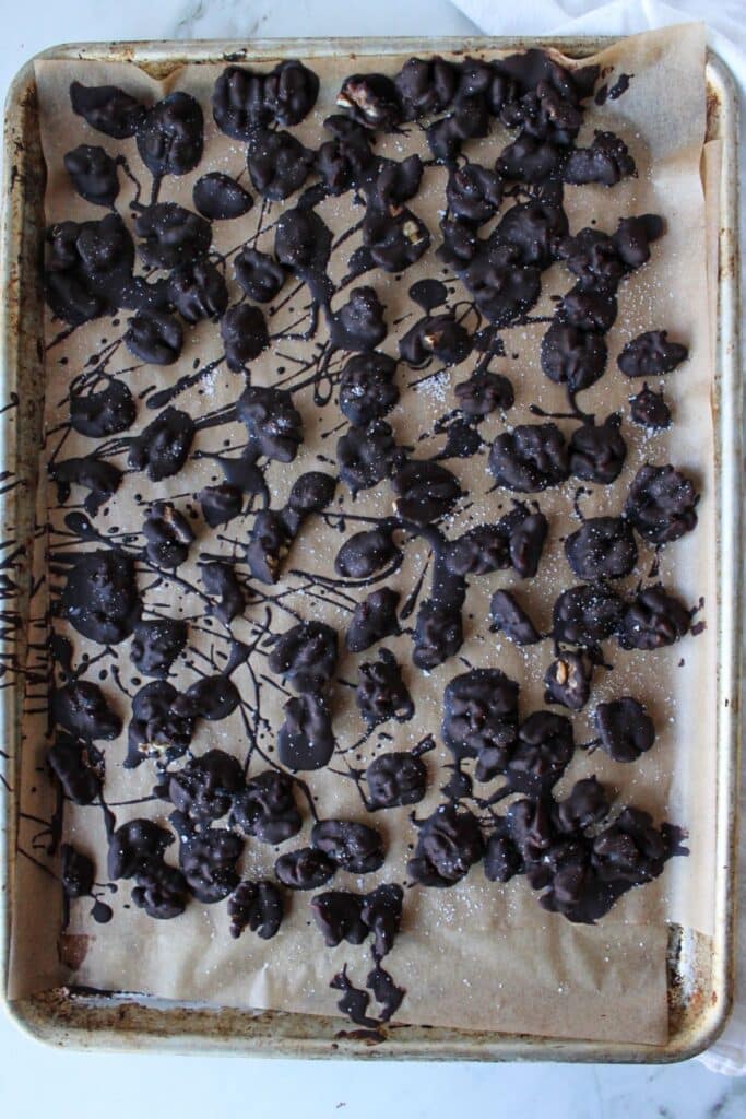 A sheet pan with parchment paper and dark chocolate covered walnuts sprinkled with flaky sea salt.
