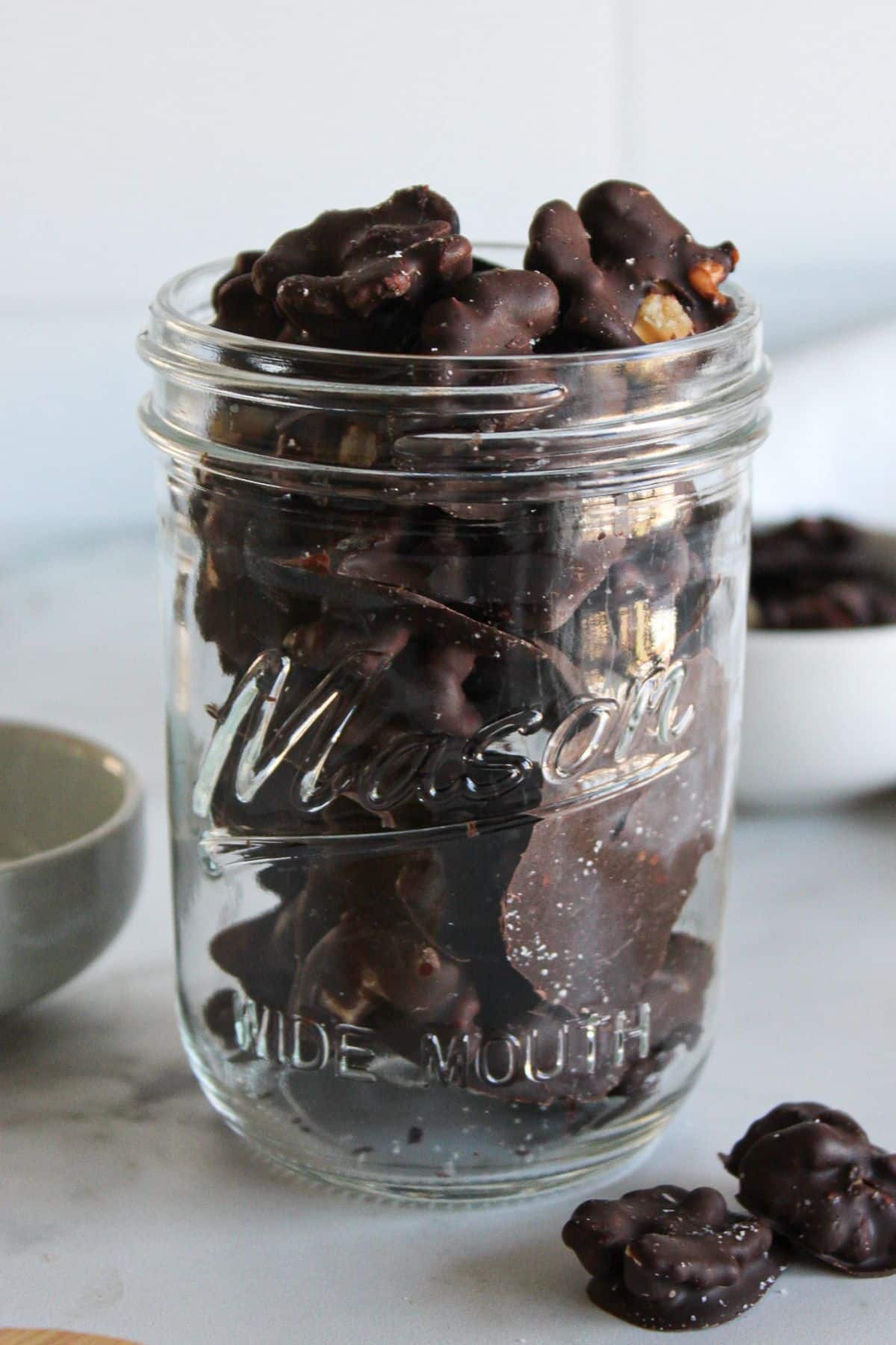 A clear glass jar of dark chocolate covered walnuts.