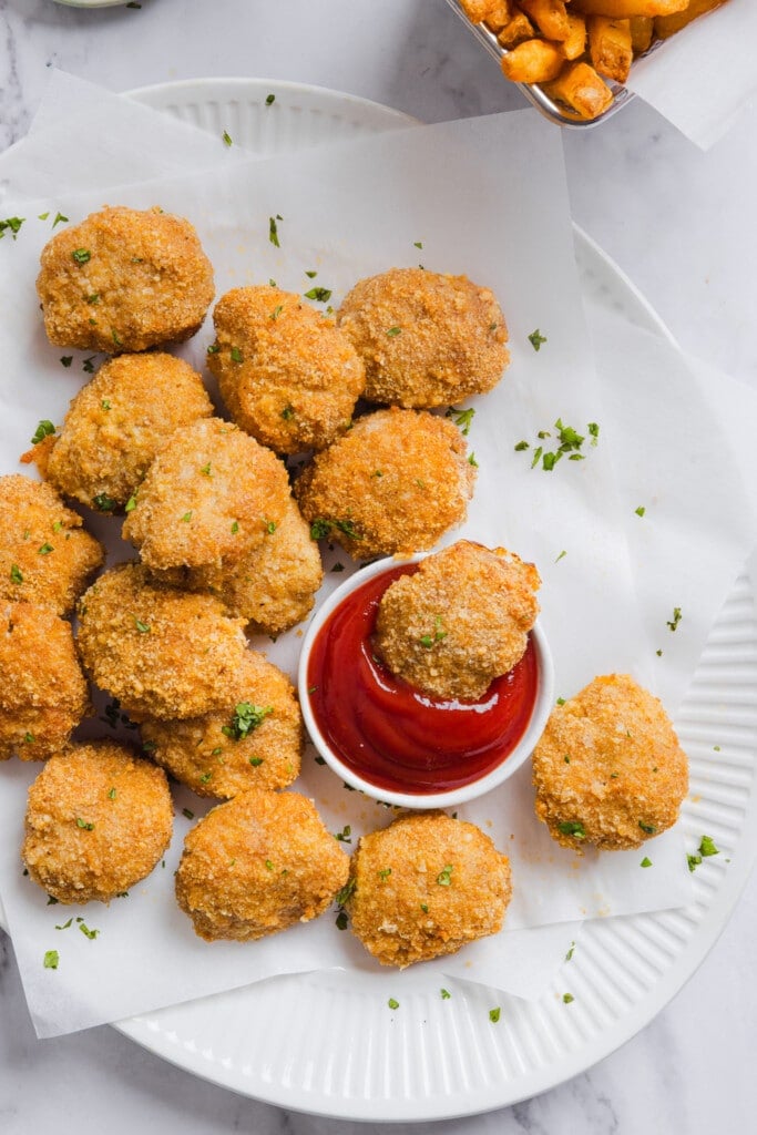 Homemade chicken nuggets on a platter with ketchup.