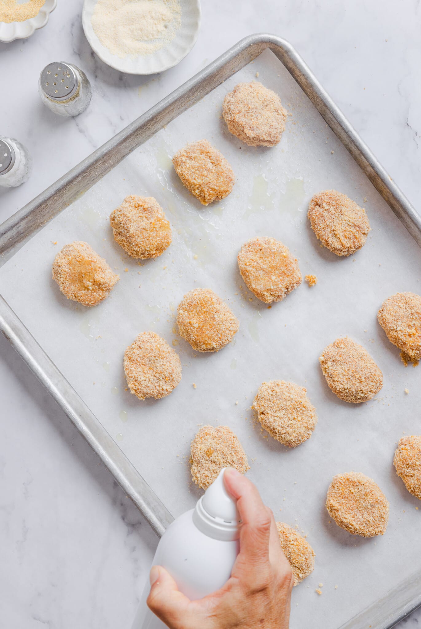 Raw ground chicken nuggets being sprayed with spray oil.
