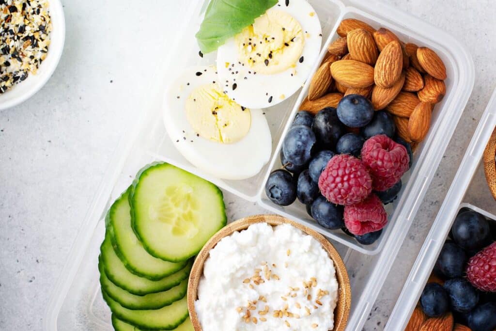 A snack box with berries, nuts, hard boiled egg, cucumber and cottage cheese.
