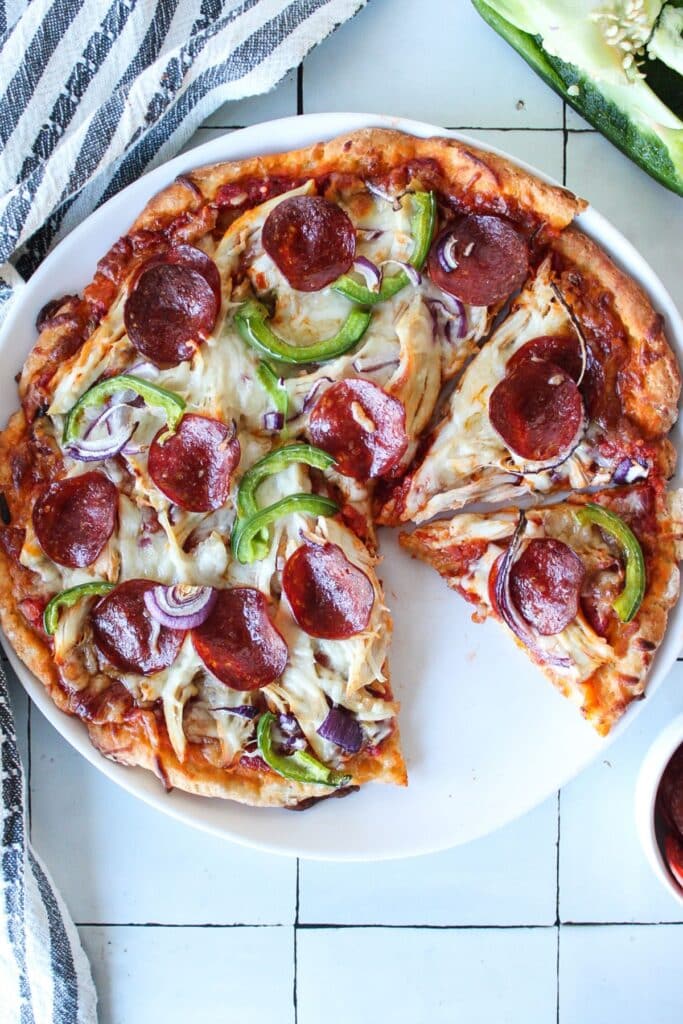 High protein pizza with two slices cut on a white plate on a countertop.