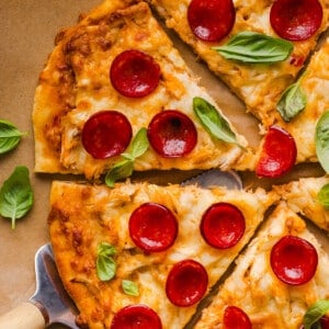 A high protein pizza sliced into slices on a brown piece of parchment paper.