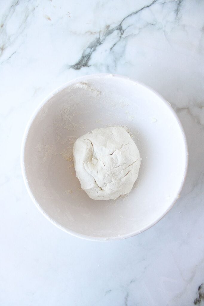 High protein pizza dough in a white bowl on a countertop.