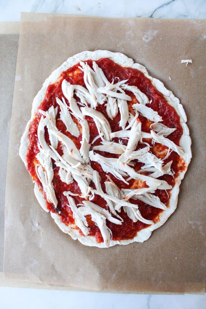 Pizza dough with pizza sauce and shredded rotisserie chicken.