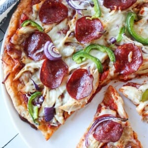 High protein pizza with two slices cut on a white plate on a countertop.