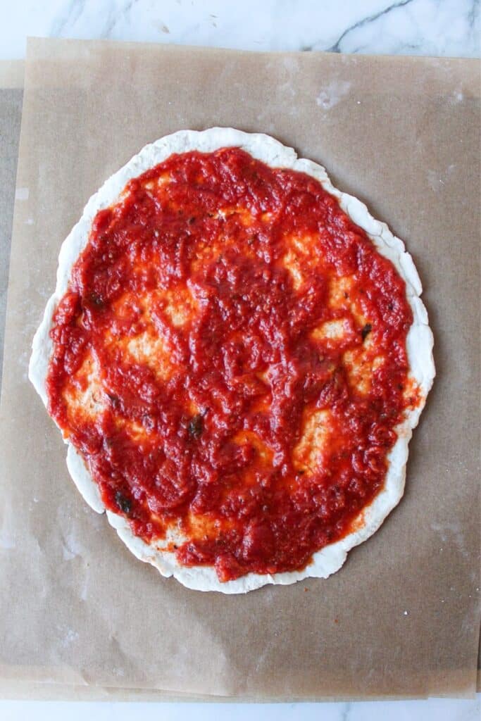 Tomato sauce on pizza dough on parchment paper.