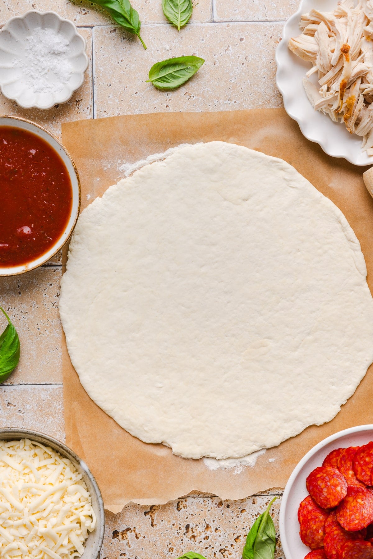 The high protein pizza crust rolled out on a piece of brown parchment paper on a countertop.