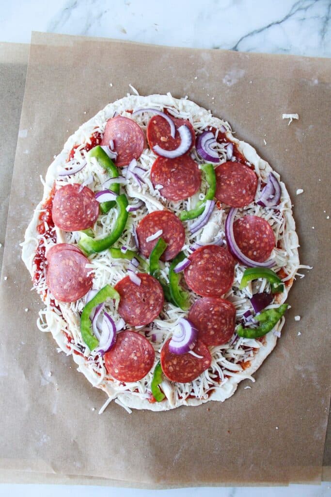 Raw high protein pizza on a piece of parchment paper ready to go into the oven.