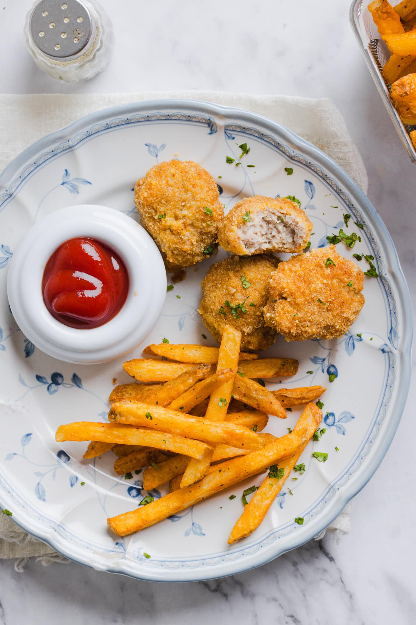 Homemade ground chicken nuggets on a plate with fries and ketchup.