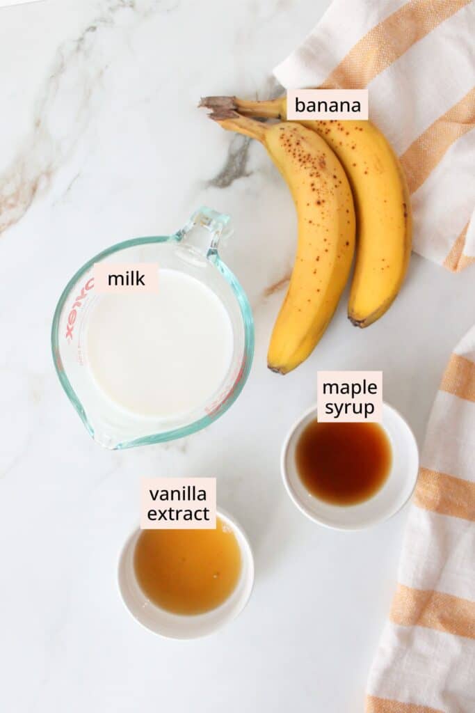 Bananas, milk, maple syrup and vanilla extract on a countertop with labels.