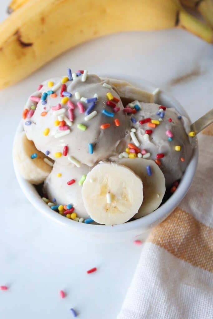 A small white bowl of Ninja creami banana ice cream with colorful sprinkles.