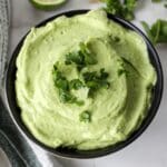 Avocado lime crema in a black bowl garnished with cilantro.