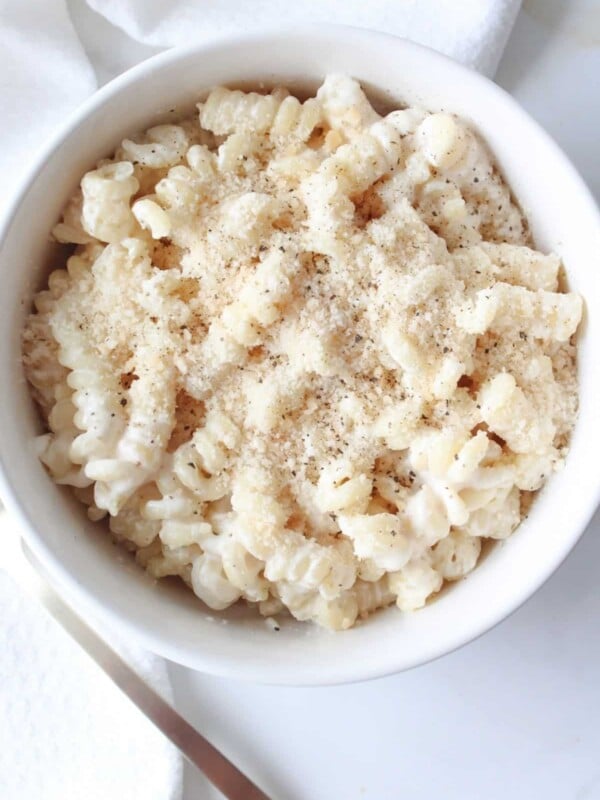 A bowl full of cottage cheese pasta sauce on chickpea pasta and topped with parmesan cheese and black pepper in a white bowl.