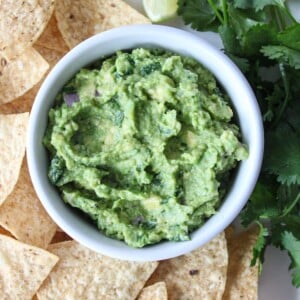 A close up shot of a white bowl of guacamole with chips.