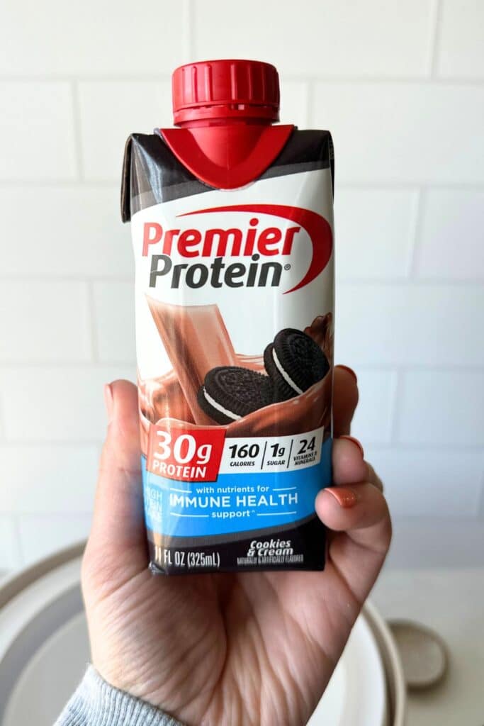 A hand holding up a premier protein shake.