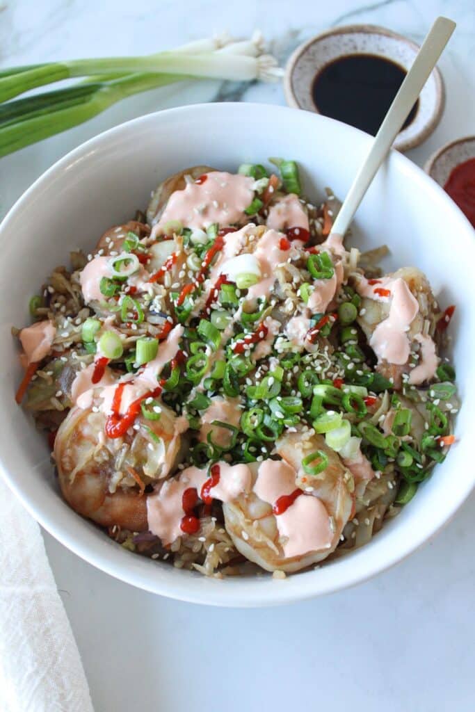 Shrimp egg roll in a bowl topped with a spicy creamy sauce and sriracha.