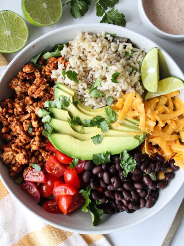 A taco rice bowl with ground turkey, rice, avocado, tomato, black beans, and shredded cheese with a creamy taco dressing on the side.