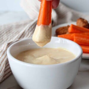 A carrot being dipped into 3 ingredient honey mustard.