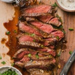Marinated cooked steak sliced on a cutting board with a small board of the marinating sauce to the side.