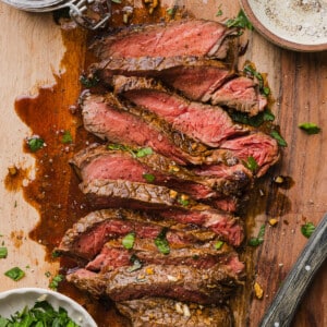 Marinated cooked steak sliced on a cutting board with a small board of the marinating sauce to the side.