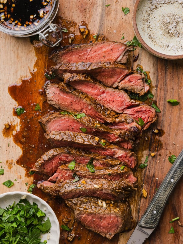 Marinated cooked steak sliced on a cutting board with a small board of the marinating sauce to the side.