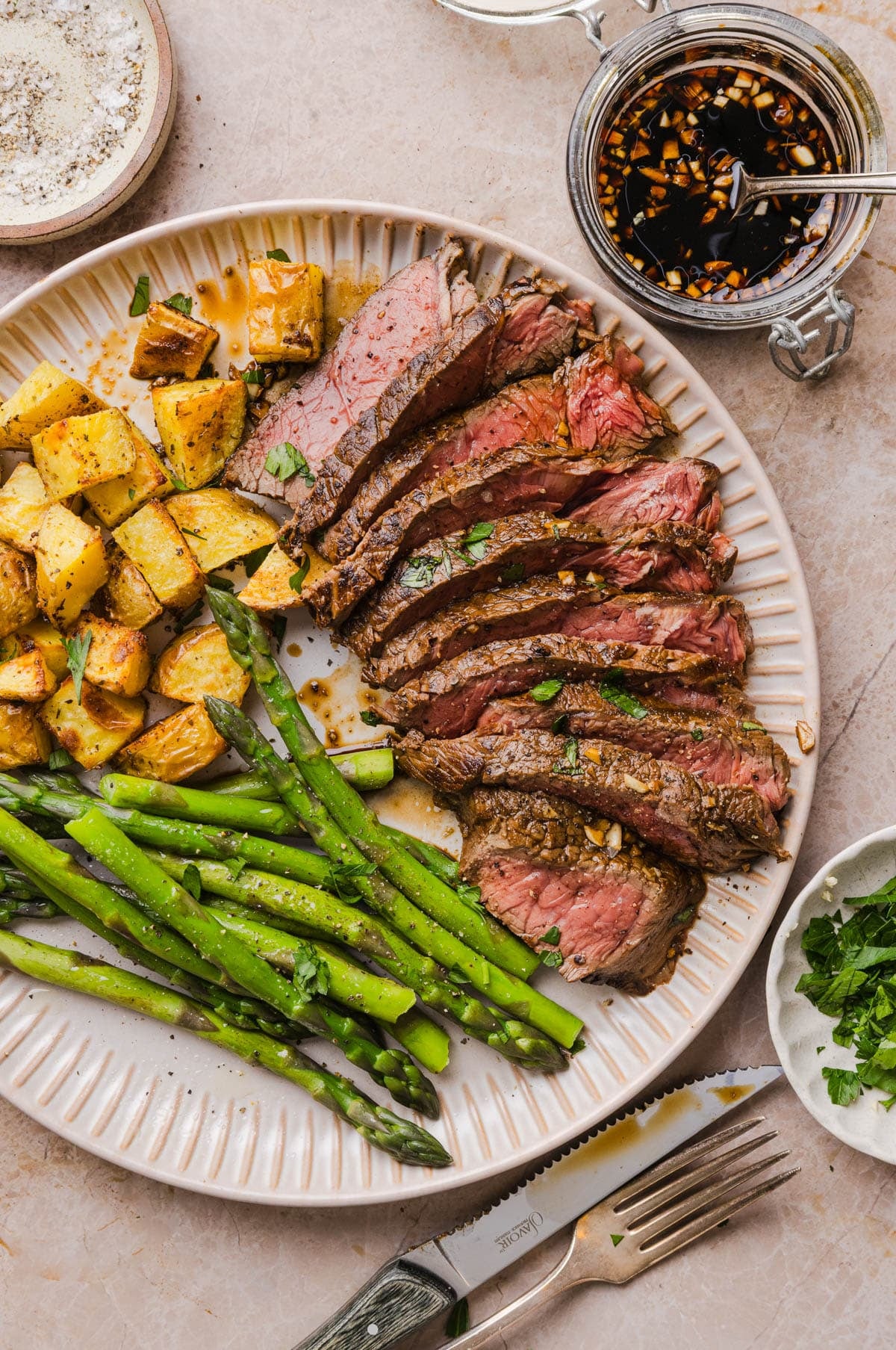 The cooked marinated steak on a plate with cooked asparagus and potatoes.