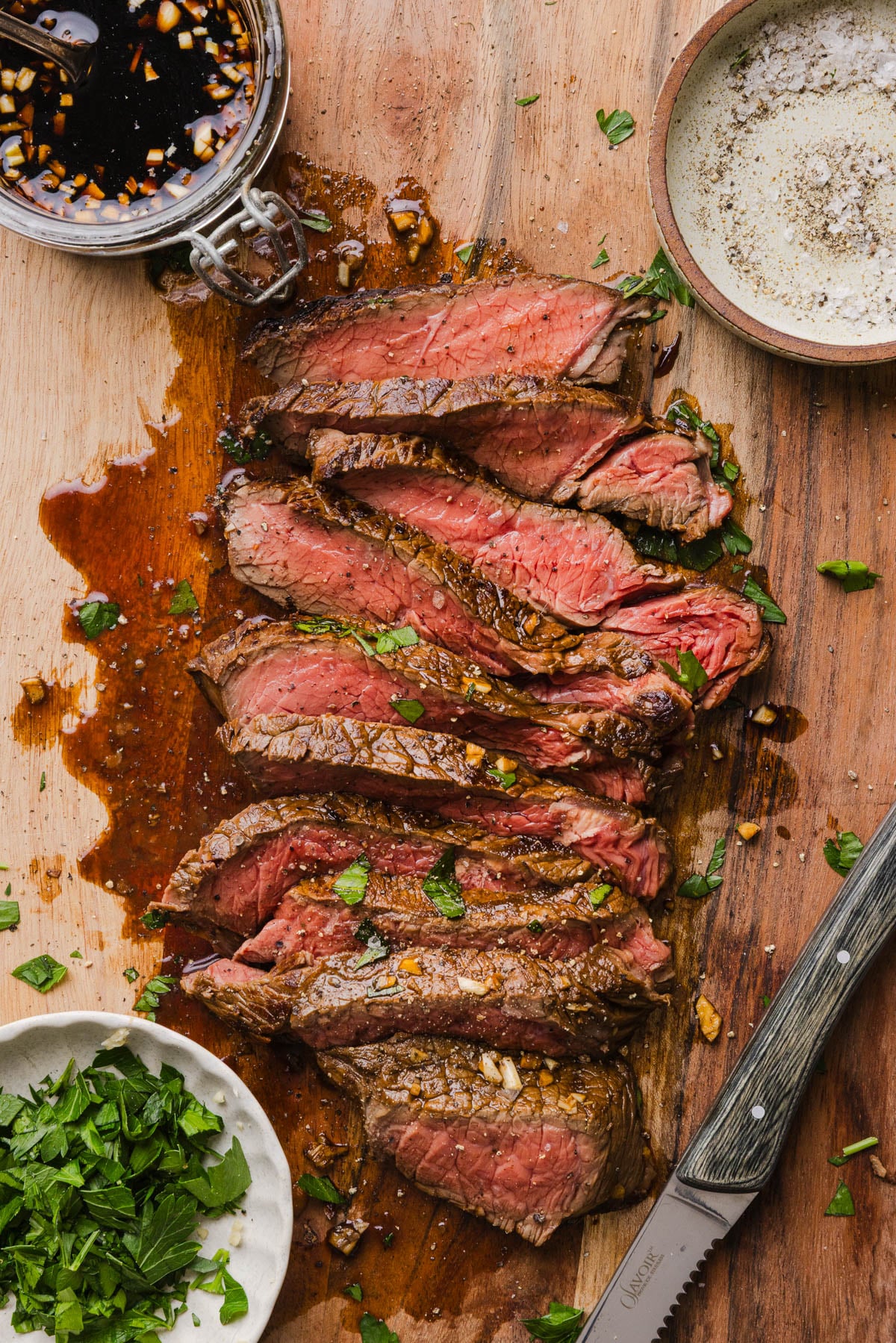 Marinated cooked steak sliced on a cutting board with a small board of the marinating sauce to the side.